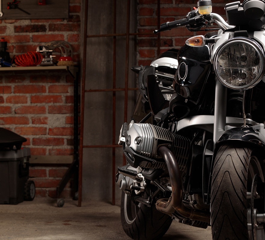 Gros plan sur un moteur Boxer noir de moto dans un garage en briques rouges avec des outils sur une étagère.