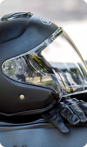 Casque Moto Noir et Gant Cuir sur Moto Casque moto noir mat Shoei avec visière transparente, reposant sur un blouson ou une selle en cuir noir, près d'un gant de moto en cuir perforé.