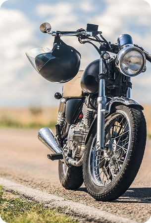 Moto Custom Classique et Casque sur Route de Campagne Moto custom chromée et noire à l'arrêt sur une route de campagne, casque noir suspendu au guidon sous un ciel bleu.