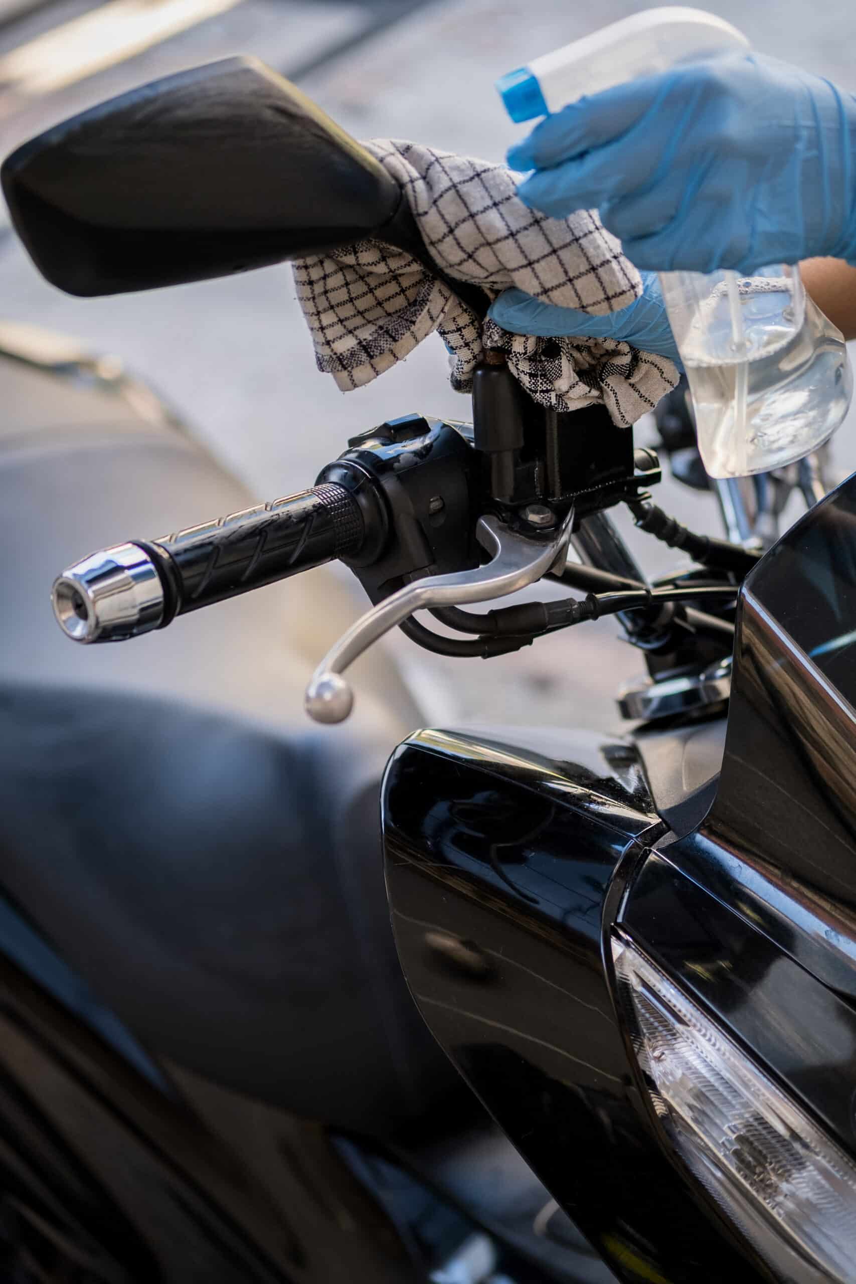 Gant bleu désinfectant guidon moto noir avec spray et chiffon à carreaux, gros plan sur la poignée.