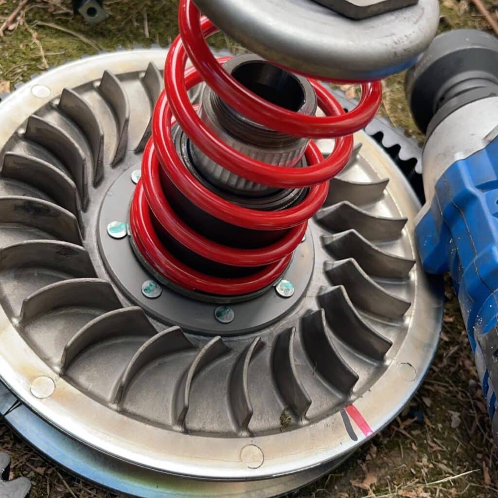 Ressort Embrayage CVT Rouge et Poulie de Transmission Ressort d'embrayage CVT rouge neuf et poulie de transmission en gros plan, outil de clé à chocs bleu à droite.