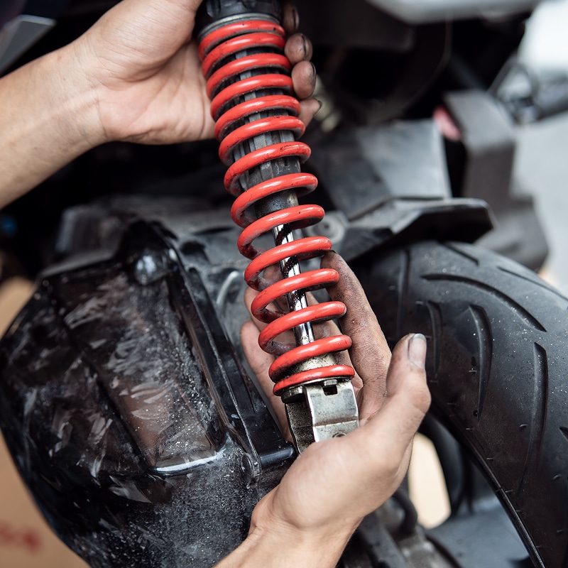 Mécanicien aux mains sales tenant un amortisseur rouge à ressort pour moto ou scooter lors d'une réparation.